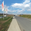 Fáze 1A – Pohled směrem od Karlovarské cesty E48 na dokončenou příjezdovou komunikaci, most, gabionové zdi, dokončené žel. stavby. V pozadí vpravo zprovozněná skladová hala.